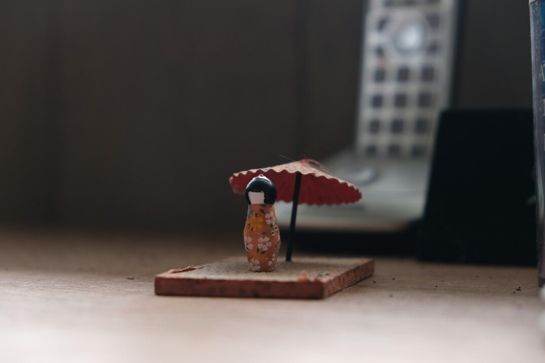 Hands of a Japanese person holding a small umbrella over a miniature house and coins
